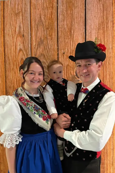 Frau, Mann und Kind in traditioneller Südtiroler Tracht vor einer Holzwand