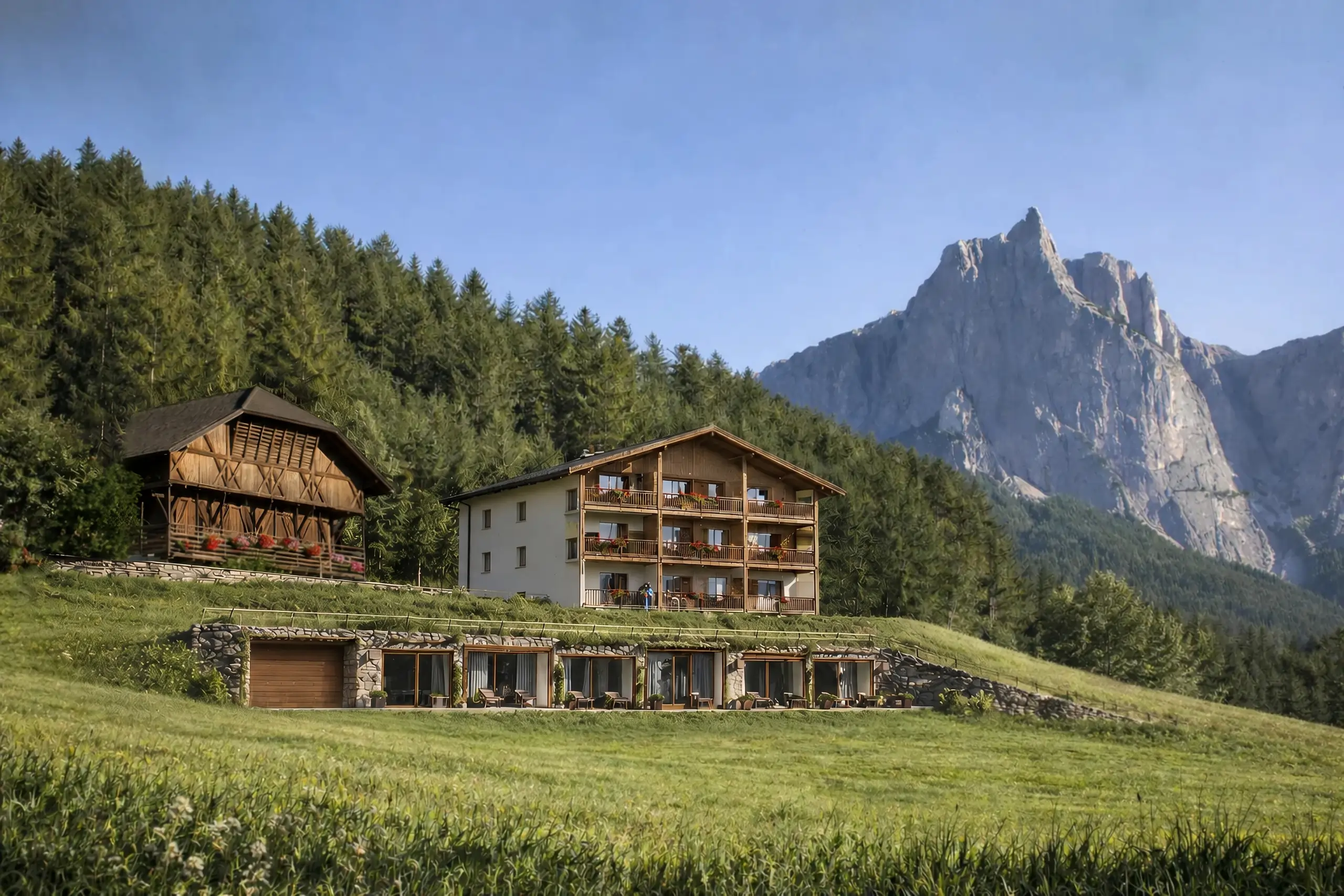 Der Unterstandroahof umgeben von grünen Wiesen und Wald mit dem Schlernmassif im Hintergrund