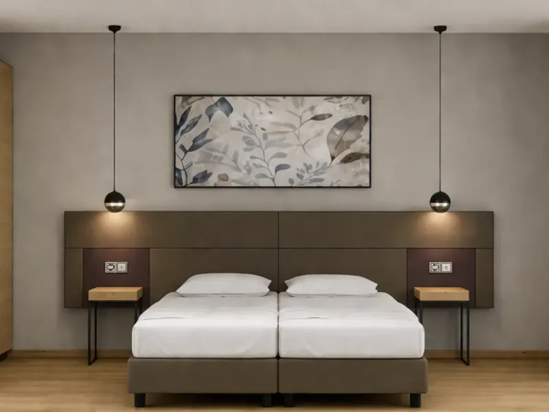 Schlicht eingerichtetes Schlafzimmer mit Doppelbett, zwei Nachttischen, hängenden Lampen und einem großen Pflanzenbild über dem Bett.